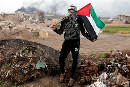 Un manifestante sostiene una bandera palestina en la escena de enfrentamientos con tropas israelíes cerca de la frontera con Israel, al este de la ciudad de Gaza