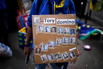 Un manifestante sostiene una pancarta con fotografías del primer ministro británico Boris Johnson, los miembros de su gabinete de gobierno y el presidente de Rusia Vladimir Putin, frente a las Casas del Parlamento, en Londres, el miércoles 6 de julio de 2022. 
