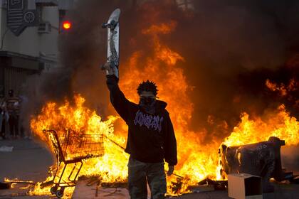 Un activista levanta su skate en señal de no agresión, con un incendio de fondo tras las marchas y la represión policial