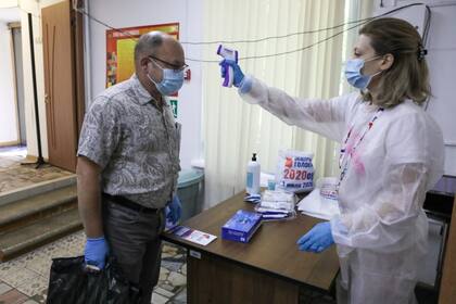 Un miembro de la comisión electoral, derecha, verifica la temperatura de un votante, ambos con máscaras faciales para protegerse contra el coronavirus en un colegio electoral en Moscú
