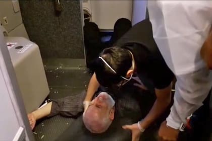 Un miembro de la tripulación ayuda a un pasajero que se cayó, luego de que el avión iraní perdiera altura