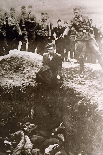 Un miembro de los Einsatzgruppen de la Gestapo, las unidades móviles especiales de matanza de los nazis, preparándose para disparar a un judío ucraniano arrodillado al borde de una fosa común