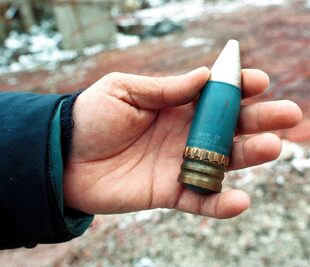 Un miembro de un equipo de radiación sostiene un proyectil perforante de 30 mm que contiene uranio empobrecido, utilizado por la OTAN durante los ataques aéreos sobre Bosnia en 1995, que fue encontrado en una antigua fábrica militar en el suburbio de Vogosca, cerca de Sarajevo, el 15 de enero de 2001. 