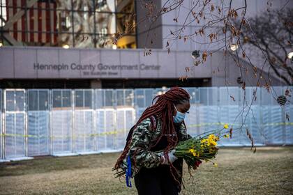 Un miembro del grupo Visual Black Justice, Daemeah Karbeh, coloca flores cerca de un árbol en el condado de Hennepin antes de que comience la selección del jurado en el juicio del exoficial de policía de Minneapolis Derek Chauvin el 8 de marzo de 2021 en Minneapolis, Minnesota