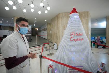 Un miembro del personal médico se encuentra junto a un árbol de Navidad hecho con envases vacíos de vacuna COVID-19 en un centro de vacunación en la capital de Rumania