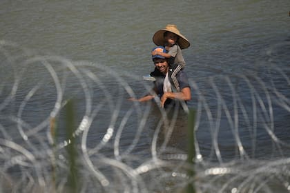 Un migrante cruza el río Bravo con un niño sobre sus hombros en un intento por llegar a Estados Unidos desde México, cerca del lugar donde trabajadores instalan una fila de boyas para que sean una barrera flotante (archivo)