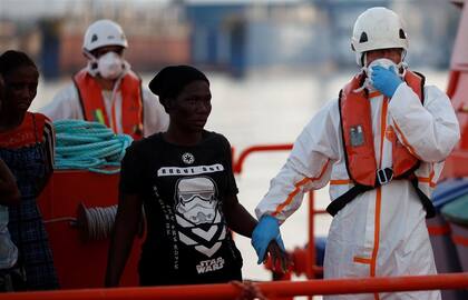 Un migrante es ayudado a descender de un barco humanitario en el Málaga