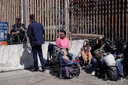 Un migrante ruso conversa con un agente fronterizo estadounidense mientras espera con otras personas el jueves 17 de marzo de 2022 en Tijuana, México, cerca del cruce limítrofe de San Ysidro, para ingresar a Estados Unidos. (AP Foto/Gregory Bull)
