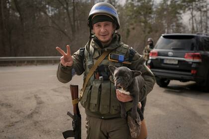 Un militar ucraniano muestra un signo de victoria sosteniendo un perro que rescató de la ciudad asediada de Irpin en las afueras de Kiev, Ucrania.