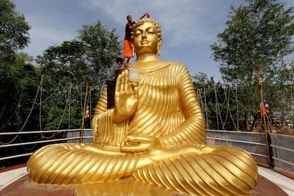Un monje budista sube a la cima de una estatua gigante de Buda, para lavar y decorarlo en la víspera de Buda Purnima, una festividad que tradicionalmente se celebra para el cumpleaños de Buda, también conocida como celebraciones de Vesak, en Bhopal