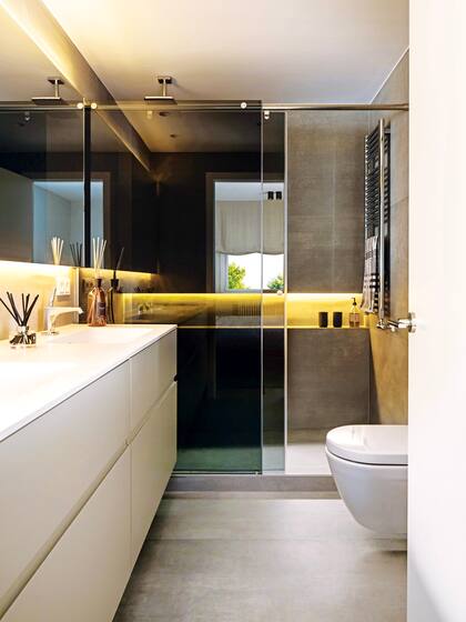 Un mueble la quedado blanco empotrado por demás minimalista ofrece buen espacio de guardado en un baño que tiene los metros justos.