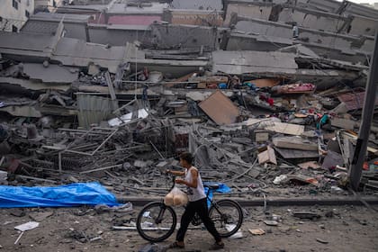 Un niño camina con una bicicleta de la mano entre los escombros de un edificio alcanzado por un ataque aéreo israelí, en Gaza