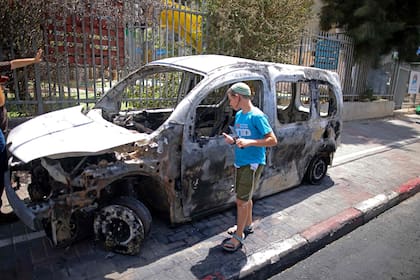 Un niño camina junto a los restos de un auto estacionado frente a una escuela religiosa judía que fue incendiada en la ciudad central israelí de Lod