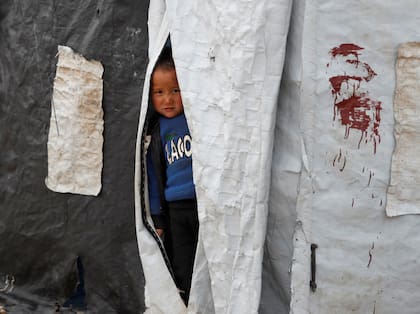 Un niño mira desde el interior de una tienda de campaña en el campamento de al-Roj