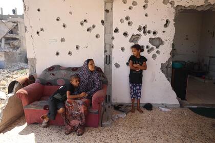 Un niño palestino abraza a una mujer y ella habla con una niña mientras está sentado en el balcón de una casa dañada en un bombardeo israelí anterior, mientras algunos residentes regresan a la ciudad de Khan Younis, en el sur de la Franja de Gaza, el 30 de junio de 2024, en medio de la conflicto en curso entre Israel y el grupo militante palestino Hamas. 