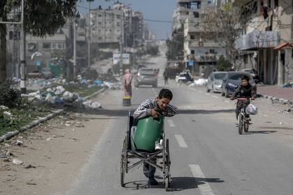 Un niño palestino transporta un contenedor de agua en silla de ruedas por una calle de la ciudad de Gaza el 3 de marzo de 2024, en medio del conflicto en curso entre Israel y el movimiento Hamas.
