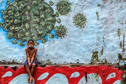 Un niño se sienta frente a un mural que representa el coronavirus en Bogor, Java Occidental, el 27 de septiembre de 2020