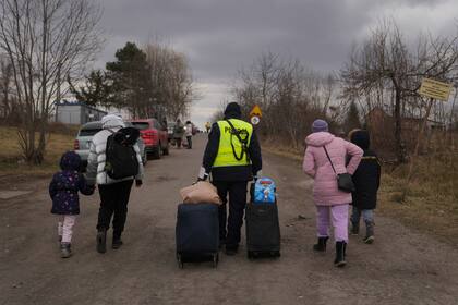 Un oficial de policía ayuda a transportar las pertenencias de las personas que han huido de Ucrania mientras caminan por el cruce fronterizo en Medyka, Polonia