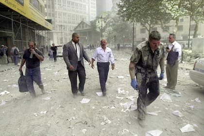 Un oficial de policía y varios ciudadanos caminan por las calles cubiertas de escombros cerca de las torres del World Trade Center