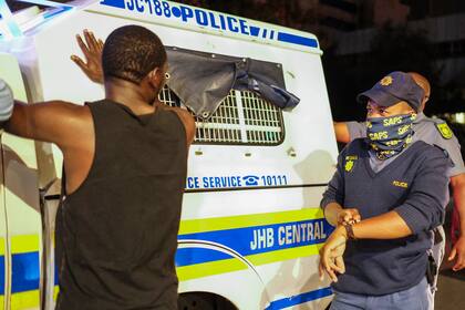 Un oficial del Servicio de Policía de Sudáfrica (SAPS) hace un gesto hacia su reloj mientras le pregunta a un peatón por qué no está en casa antes del nuevo toque de queda, para ayudar a frenar la propagación del Covid-19, en Johannesburgo el 29 de diciembre de 2020