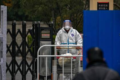 Un operario, con un traje de protección, lleva comida hasta un vecindario aislado tras la detección de un caso de COVID-19, en Beijing