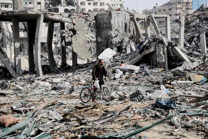 Un palestino empuja su bicicleta entre los escombros de los edificios destruidos en la ciudad de Gaza, en el norte de la franja de Gaza, tras semanas de bombardeos israelíes, mientras entraba en vigor un alto el fuego de cuatro días el 24 de noviembre de 2023. 