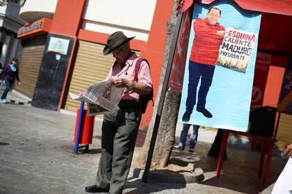 Un partidario del gobierno lee un diario que se encuentra al lado de un cartel en el que aparece el fallecido presidente de Venezuela, Hugo Chávez