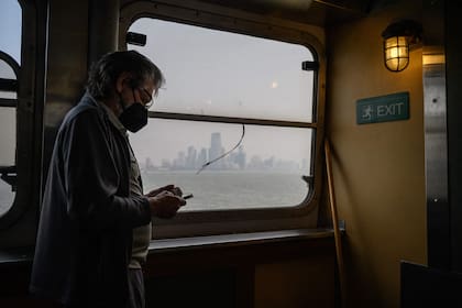 Un pasajero con una máscara facial viaja en el ferry de Staten Island más allá del horizonte de Manhattan durante una fuerte niebla en Nueva York 