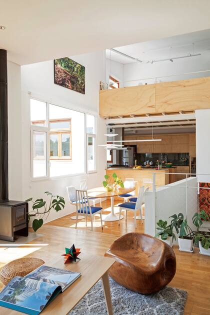 Un pequeño desnivel refuerza la transición entre el living y el comedor, con mesa 'Tulip' con tapa ovalada de madera y sillas con tapizado azul que combinan el modelo 'Tulip' con otras tipo Windsor. En primer plano, asiento tallado en madera del escultor Jorge Michel.