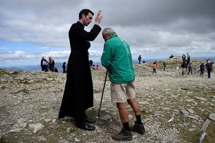 Un peregrino es bendecido por el recién ordenado padre Gerard Quirke después de la Misa en la cumbre de la montaña santa Croagh Patrick