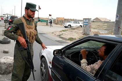 Un policía afgano habla con un viajero en automóvil en un puesto de control a lo largo de la carretera en Kabul el 14 de agosto de 2021 (Foto de WAKIL KOHSAR / AFP).