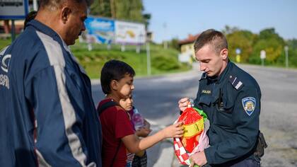 Un policía corta entrega víveres a inmigrantes en el paso fronterizo de Bregana, frente al límite con Eslovenia