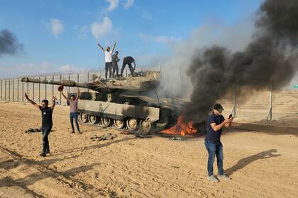Un puñado de palestinos celebran junto a un tanque israelí desarticulado tras la veloz invasión del 7 de octubre al sur del país 