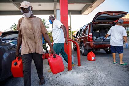 Un residente camina con contenedores llenos de gasolina en la estación de servicio de Cooper antes de la llegada del huracán Isaias a Freeport, Gran Bahama, Bahamas,