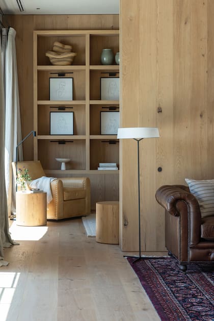 Un rincón de lectura que invita a relajarse, con una apuesta total por los tonos claros, desde el sillón y los bancos hasta la biblioteca (con retratos de Francesca Molinari) y las paredes revestidas de madera.