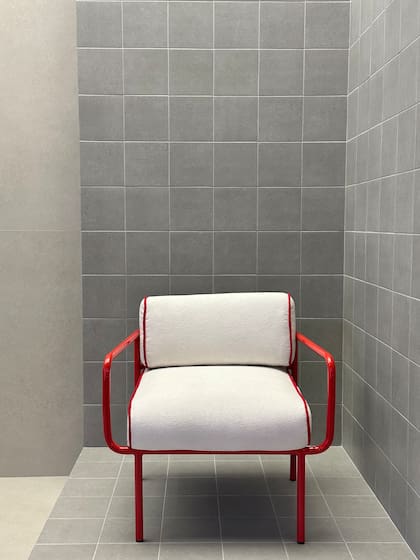 Un rincón minimalista donde los revestimientos grises enmarcan una silla de líneas rojas, resaltando el juego entre textura neutra y acento de color en la feria.