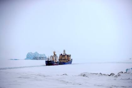 Un rompehielos que abre el camino para un carguero con un iceberg al fondo cerca de un puerto en la isla Alexandra Land