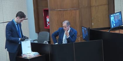 Un secretario del tribunal le exhibe los cuadernos originales al periodista