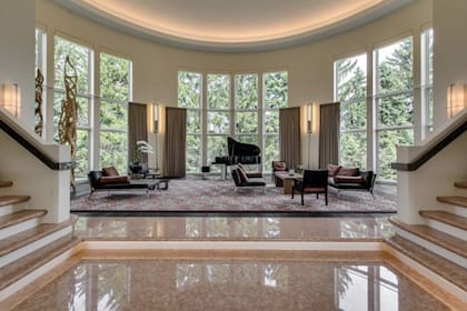 Un señorial living con sillones, piano y dos escaleras que llevan a diferentes alas de la casa