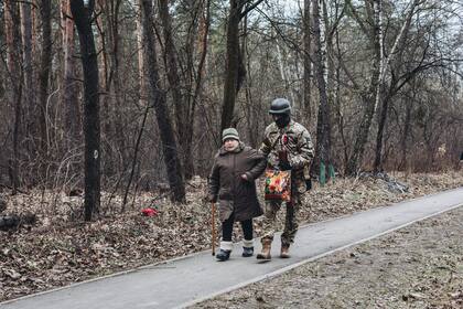 Un soldado ayuda a camina a una anciana bajo el bombardeo ruso a la ciudad de Irpin luego de que el ejército ruso violara el alto el fuego pactado, el 6 de marzo de 2022