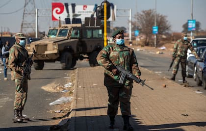 Un soldado observa mientras los líderes comunitarios hablan a un grupo de hombres en un esfuerzo por evitar que entren en un centro comercial en Vosloorus, al este de Johannesburgo, Sudáfrica.