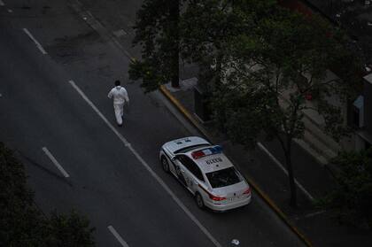 Un trabajador, con equipo de protección personal (EPP), camina junto a un coche de policía en una calle durante un cierre de COVID-19 en el distrito de Jing'an en Shanghai el 11 de abril de 2022