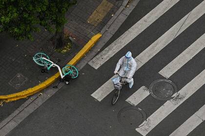 Un trabajador con equipo protector anda en bicicleta por las calles de Shanghái