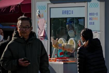 Un trabajador con ropa de protección desinfecta sus guantes mientras la gente se hace pruebas rutinarias de COVID-19 en Pekín, China, el jueves 8 de diciembre de 2022.