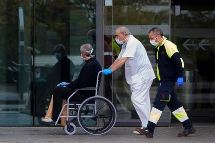 Un trabajador de la salud empuja a un paciente en una silla de ruedas frente al hospital La Fe el 25 de marzo de 2020, en Valencia