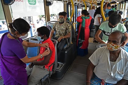 Un trabajador de la salud inocula contra el coronavirus a un trabajador en un autobús convertido en un centro de vacunación móvil en la India