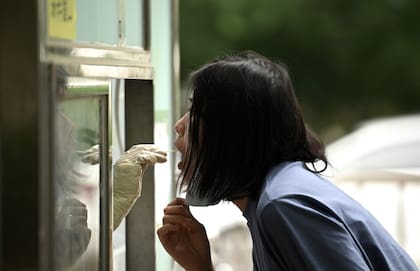 Un trabajador de la salud (izq.) se asoma por una ventana para tomar una muestra de hisopo de una mujer para hacerle la prueba del Covid-19 en Pekín el 9 de junio de 2022. (Photo by Noel Celis / AFP)