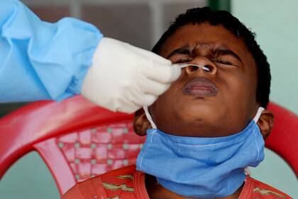 Un trabajador de la salud toma una muestra de hisopado de un niño para la prueba de RT PCR y antígeno rápido del coronavirus en un centro de pruebas en Chennai el 19 de diciembre de 2020, cuando India superó los 10 millones de casos de coronavirus