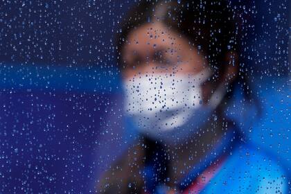 Un trabajador enmascarado camina junto a una ventana cubierta por la lluvia después de una tormenta de lluvia en un partido de hockey sobre césped en los Juegos Olímpicos de Verano de 2020, el martes 27 de julio de 2021, en Tokio, Japón.