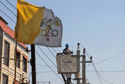 Un trabajador iraquí arregla cables eléctricos mientras la bandera del Vaticano ondea frente a la iglesia católica caldea de San José, antes de la visita del Papa Francisco, en la capital Bagdad, el 26 de febrero de 2021